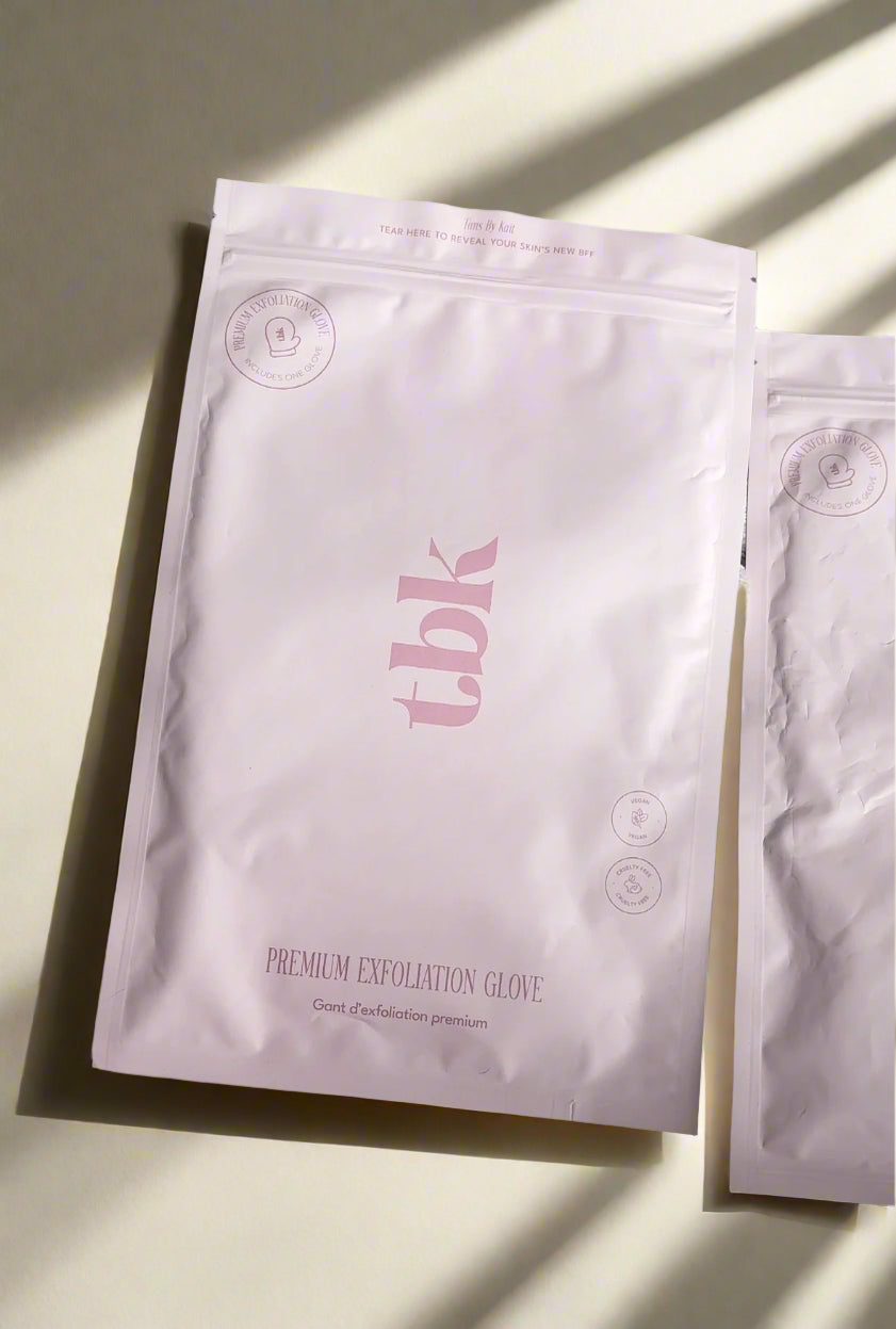 Two packages of Tans By Kait's premium exfoliation gloves on a light background